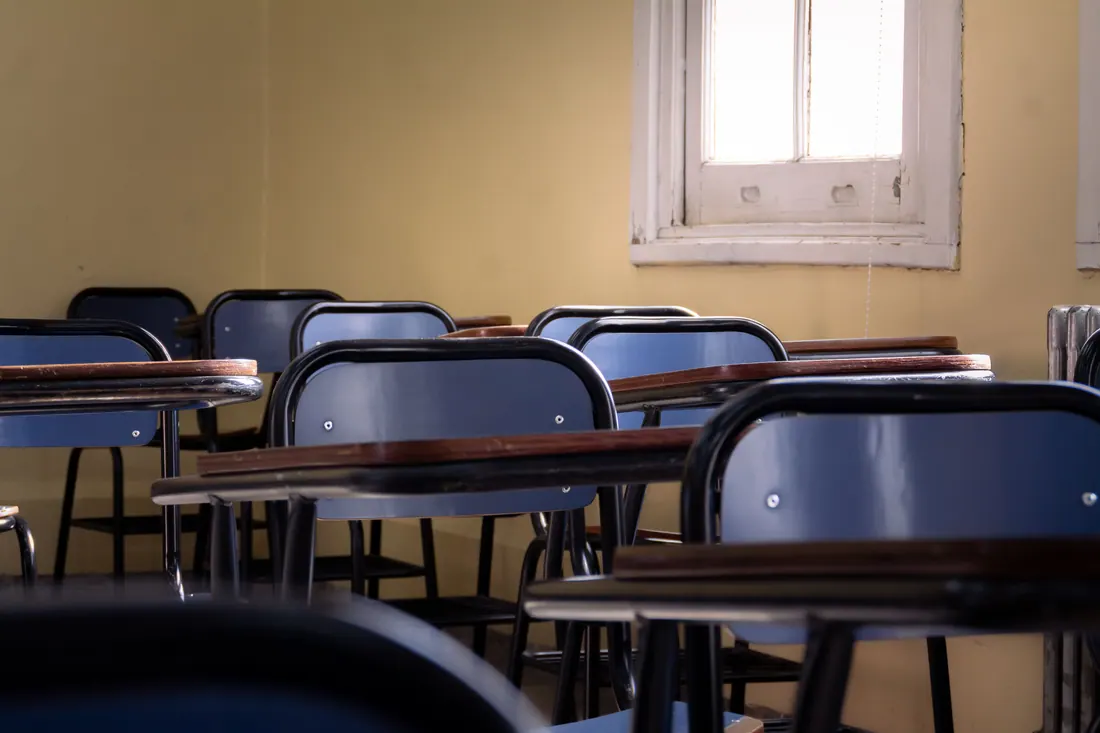 Pupitres vacíos en un aula iluminada por una ventana