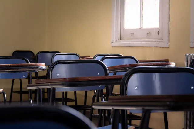 Pupitres vacíos en un aula iluminada por una ventana