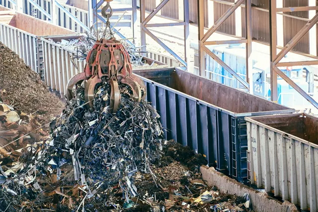 Grúa con pinza recogiendo chatarra en una planta de reciclaje