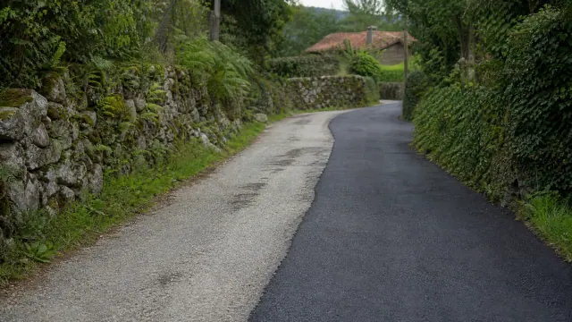 Camino rural con pavimento de grava y asfalto, flanqueado por muros de piedra