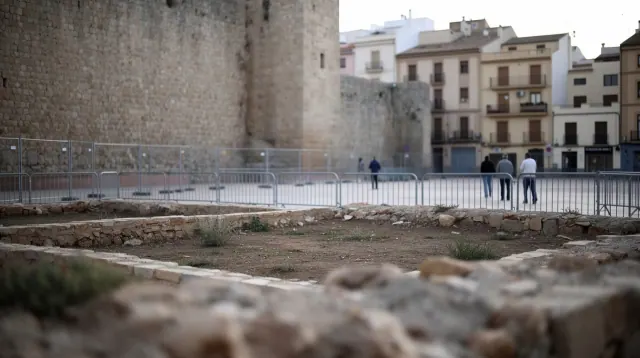 Personas caminan frente a una zona vallada en obras en una plaza de pueblo medieval