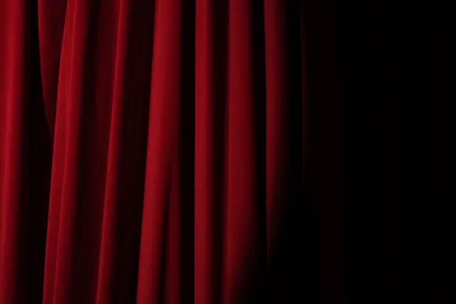 Un pesado telón de terciopelo rojo con pliegues sobre fondo oscuro