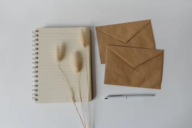 Cuaderno, sobres de papel kraft y un bolígrafo sobre una mesa