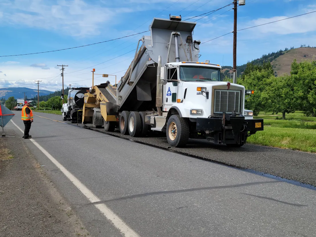 Camino rural con firme de asfalto recién extendido y vallas de obra en el arcén