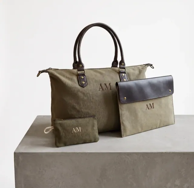Un conjunto de bolsos y neceser en lona verde con las iniciales "AM