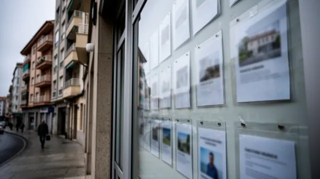 Escaparate de inmobiliaria con fotografías de propiedades en una calle urbana