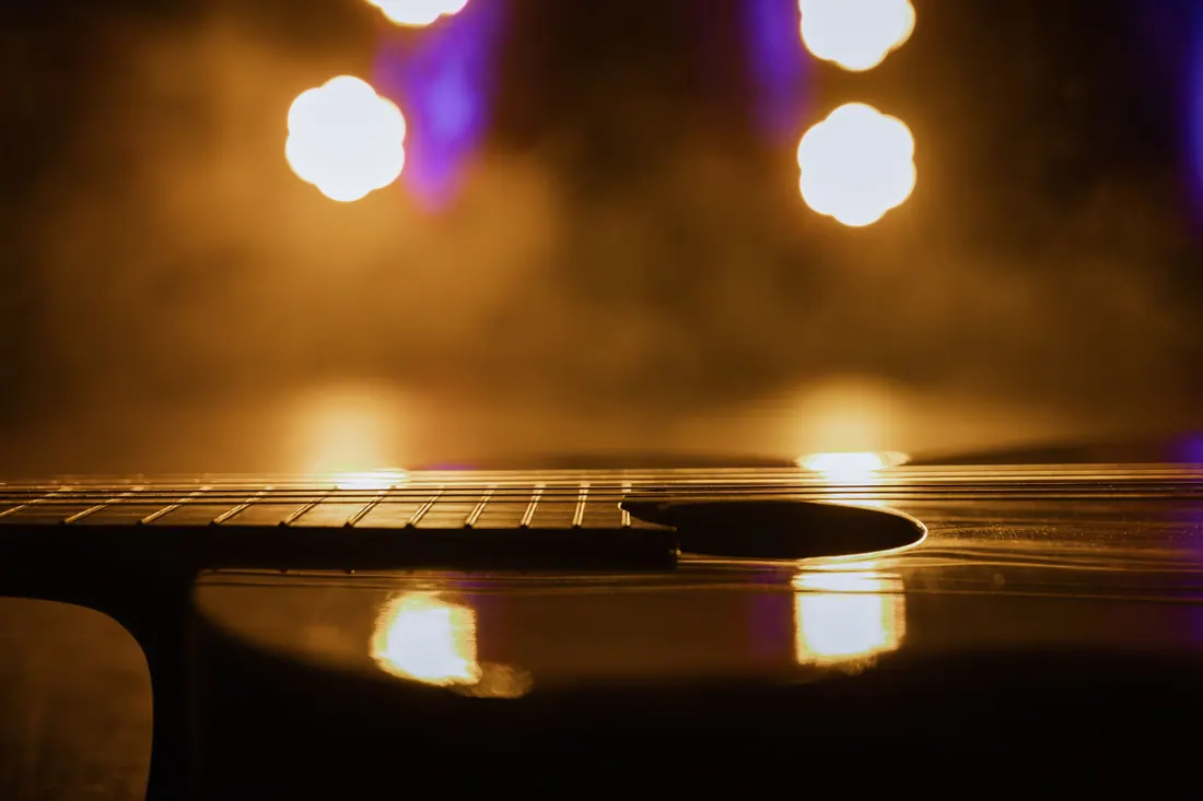 Primer plano de una guitarra acústica con luces de escenario desenfocadas