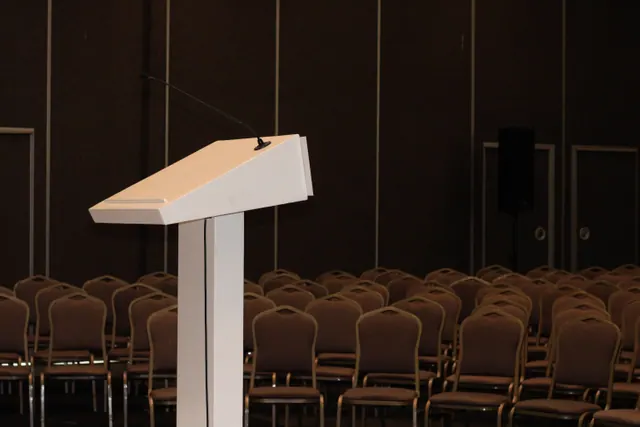Sala de conferencias vacía con un atril y filas de sillas preparadas para un acto