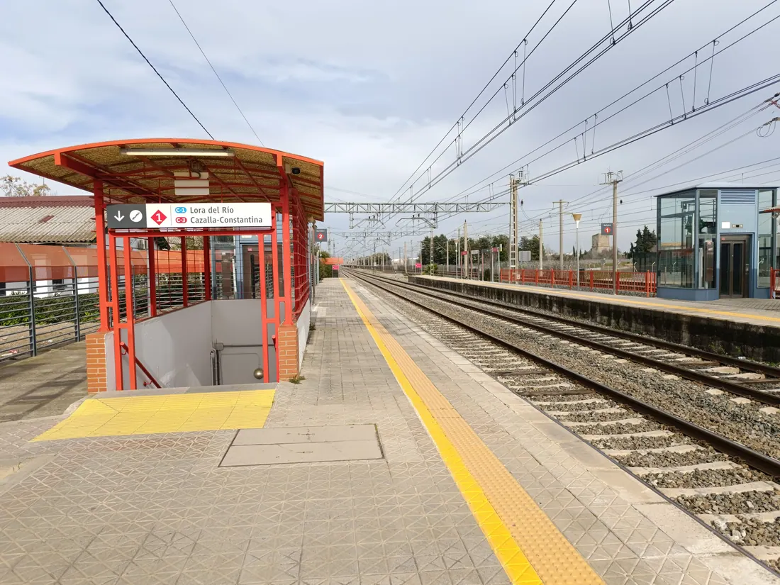 Andén de una estación de tren con indicaciones hacia Lora del Río