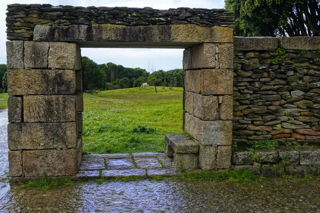 Portalón de piedra en un muro que da a un prado verde