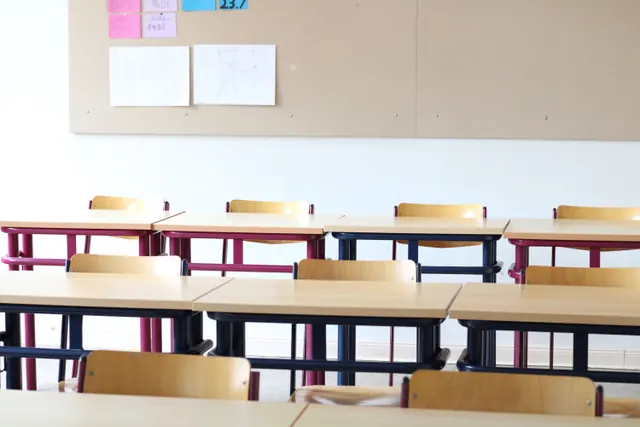 Aula vacía con pupitres y sillas ordenados en filas junto a un panel con notas
