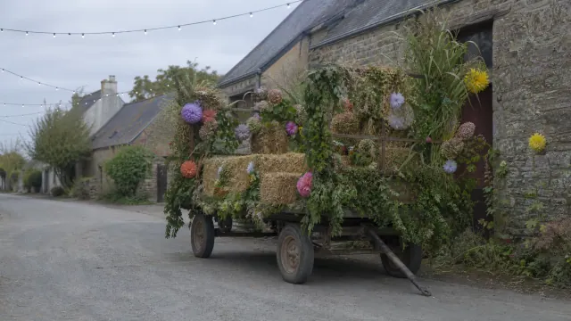 Carro de madera cubierto de plantas y flores coloridas junto a casas de piedra