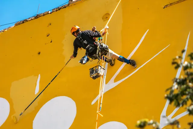 Artista pintando un gran mural en la fachada de un edificio urbano