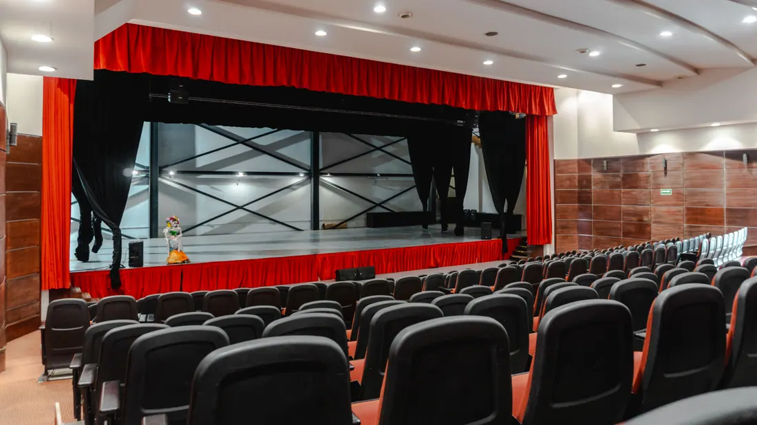 Sala de teatro vacía con el telón rojo abierto sobre el escenario