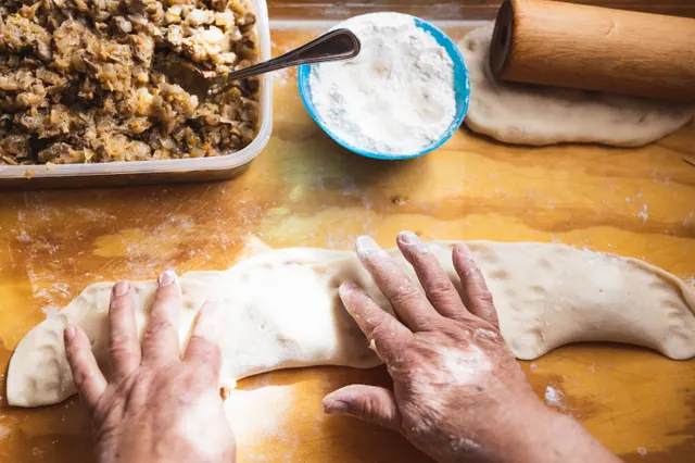 Unas manos preparan empanadas rellenas sobre una mesa de madera
