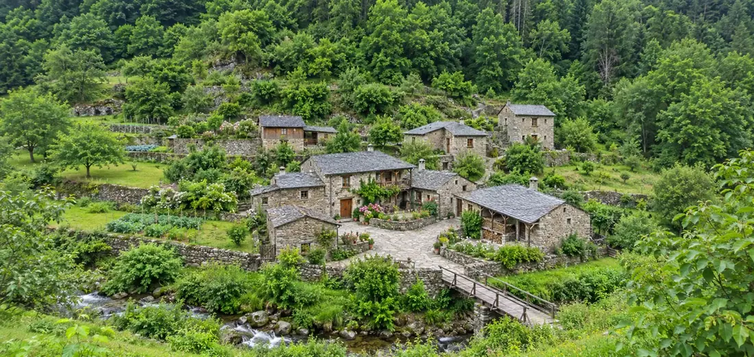 Aldea de casas de piedra con tejados de pizarra sobre un arroyo