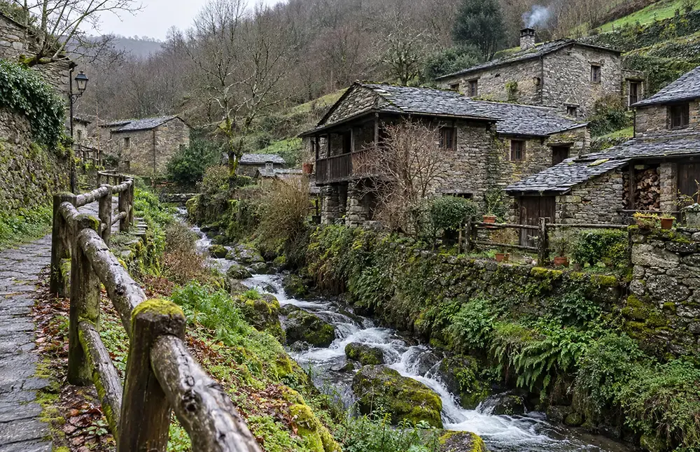 Arroyo encajado entre casas de piedra, con una barandilla de madera en primer plano
