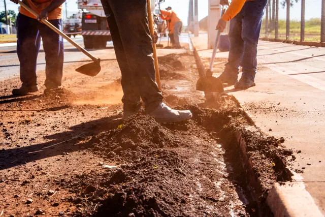 Trabajadores cavando una zanja en una acera con tierra roja