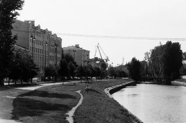 Paseo junto a un canal urbano con edificios y grúas al fondo