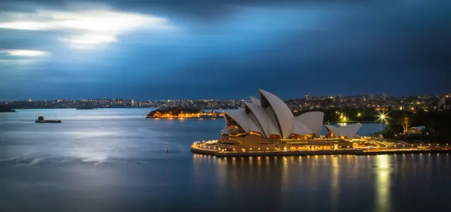 La Ópera de Sídney iluminada al anochecer junto a la bahía