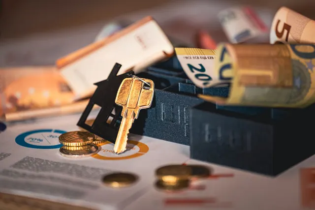 Llave con forma de casa sobre billetes y monedas de euro