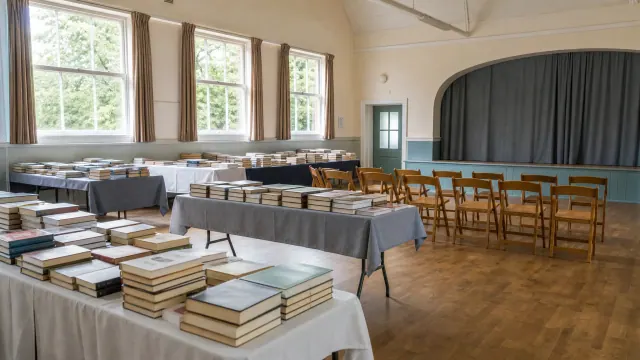 Sala con mesas cubiertas de libros y sillas de madera dispuestas