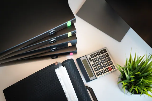 Carpetas de oficina, una calculadora y una planta sobre un escritorio