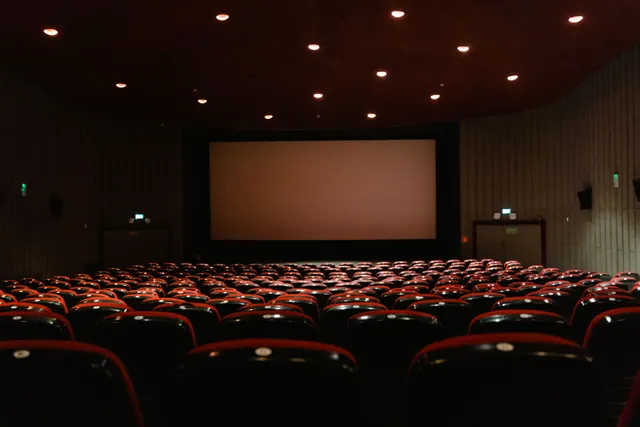 Sala de cine vacía con butacas rojas y pantalla en blanco