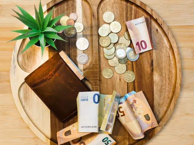 Cartera con billetes y monedas de euro sobre una bandeja de madera