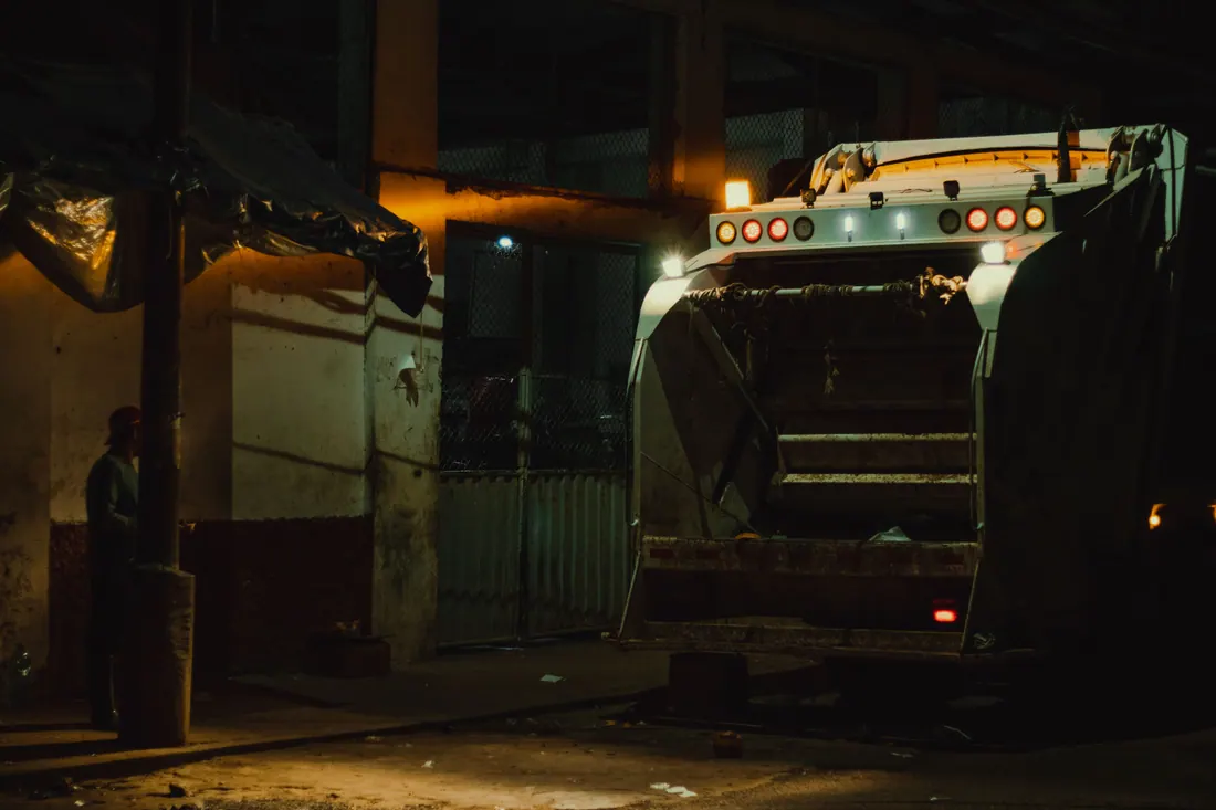 Camión de basura estacionado de noche junto a una nave industrial