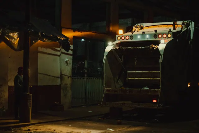 Camión de basura estacionado de noche junto a una nave industrial