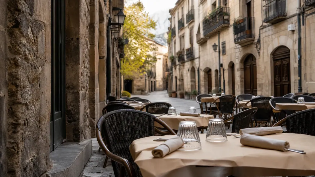 Terraza de restaurante en una plaza medieval amurallada con mesas, sillas de ratán