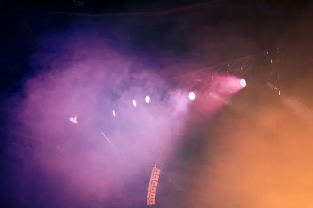 Focos y humo iluminando un escenario en un concierto nocturno